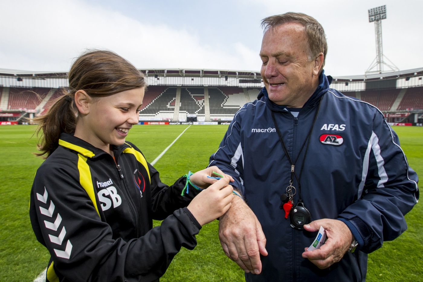 Teilnehmerin des Projekts Football for Friendship bindet Dick Advocaat das Freundschaftsarmband beim Internationalen Fußball- und Freundschaftstag um. Niederlande, 25. April 2014